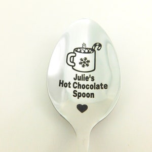May include: A silver spoon with a black engraved design of a mug of hot chocolate with marshmallows and a candy cane, along with the text "Julie's Hot Chocolate Spoon" and a small heart.