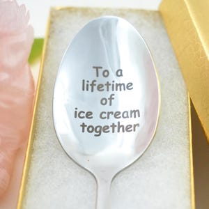 Puede incluir: Una cuchara de plata con la inscripci&oacute;n "To a lifetime of ice cream together". La cuchara est&aacute; en una caja blanca con un borde dorado.