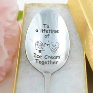 Puede incluir: Una cuchara de plata con las palabras "To a lifetime of Ice Cream Together" grabadas en ella. La cuchara est&aacute; en una caja con una tapa dorada.