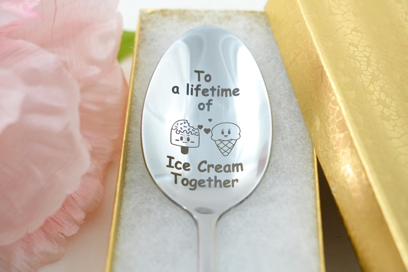Puede incluir: Una cuchara de plata con las palabras "To a lifetime of Ice Cream Together" grabadas en ella. La cuchara est&aacute; en una caja con una tapa dorada.