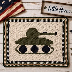 May include: A rectangular crochet blanket featuring a central olive green tank design on a cream background. The blanket has a multi-colored border in dark navy, olive green, and tan. The tank has three dark navy circular wheels.