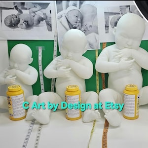 May include: Three white realistic baby dolls with closed eyes and hands clasped together. The dolls are sitting on a green surface with a measuring tape. Each doll is holding a yellow bottle with a white label.