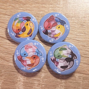 Peut inclure: Quatre badges ronds bleus avec un motif de poisson de dessin animé. Chaque bouton représente deux poissons dans un style yin-yang, avec différentes combinaisons de couleurs, dont arc-en-ciel, rouge/jaune, rose/orange et vert/noir.