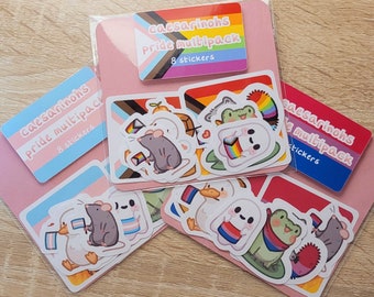 May include: A collection of Pride multipack stickers featuring various designs. The stickers include cute animal illustrations such as a rat, duck, and frog, each holding or wearing Pride flags. The packs are labeled with the text "caesarinhs Pride multipack 8 stickers".