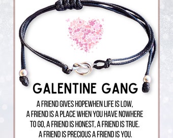 May include: Black friendship bracelet with a silver-toned knot clasp and adjustable sliding knots. The text "GALENTINE GANG" is displayed, along with a quote about friendship. A pink heart made of flowers is also shown.