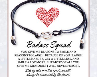 May include: Black friendship bracelet with a silver-toned knot clasp and adjustable sliding knots. The card behind the bracelet has a red heart made of smaller hearts and the text "Badass Squad".