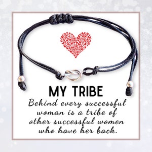 May include: Black friendship bracelet with a silver infinity knot charm and silver beads. The bracelet has a red heart with smaller hearts inside. The text "MY TRIBE" is printed in black, followed by the quote "Behind every successful woman is a tribe of other successful women who have her back."