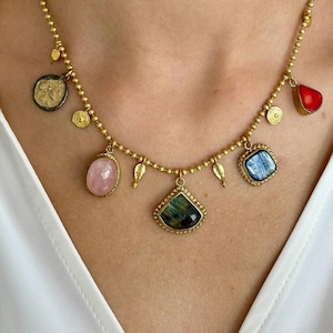 May include: Gold-toned necklace featuring various gemstone pendants, including a pink oval, a blue square, and a green and black triangular stone. The necklace also has coin and leaf charms.