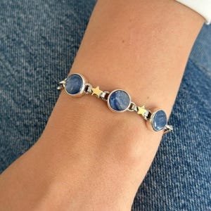 Puede incluir: Una pulsera de plata con tres piedras preciosas azules redondas y detalles de estrellas doradas. Las piedras están engastadas en biseles de plata. La pulsera está unida con pequeñas cadenas de plata.