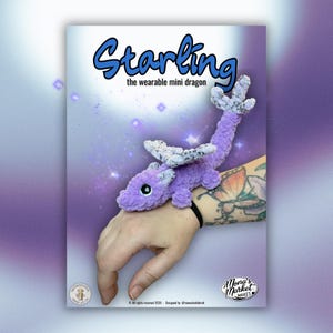 May include: A purple crochet dragon toy with white and gray wings, labeled "Starling the wearable mini dragon." The dragon is resting on a person's wrist. The background is a gradient of purple and white with star accents.