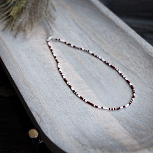 May include: A white and burgundy beaded necklace on a wooden surface.