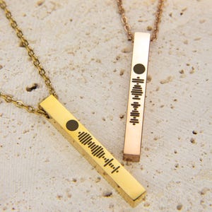 May include: Two gold bar necklaces with a soundwave design. The necklace on the left is gold and the necklace on the right is rose gold.