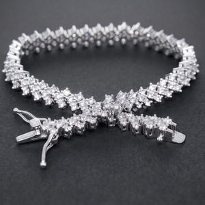 May include: A silver-toned tennis bracelet featuring multiple rows of small, clear, round-cut stones set in a metallic frame. The bracelet includes a secure box clasp mechanism with a safety latch, creating a continuous, sparkling, circular design.