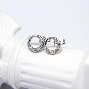 May include: A pair of silver stud earrings with a circle design. The circle is outlined with small clear stones.