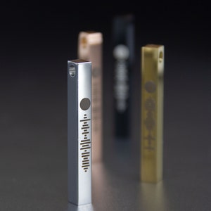 May include: Three silver, gold, and black metal bar pendants with a sound wave design. The silver pendant is in focus and has a circle at the top.