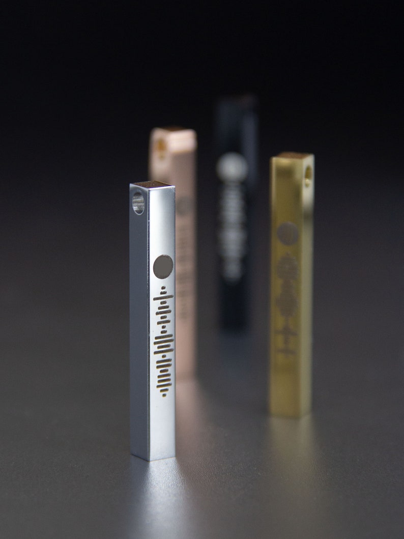 May include: Three silver, gold, and black metal bar pendants with a sound wave design. The silver pendant is in focus and has a circle at the top.