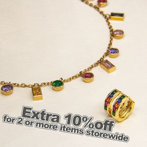 Puede incluir: Un collar de cadena dorada con piedras preciosas de colores y dijes rectangulares. El collar está sobre un fondo blanco. También se muestra un arete de aro dorado con piedras preciosas de colores.  Descuento adicional del 10% en la compra de 2 o más artículos en toda la tienda.
