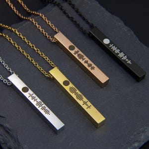 May include: Four necklaces with different coloured chains and bar pendants featuring a unique soundwave design. The chains are silver, gold, rose gold, and black.