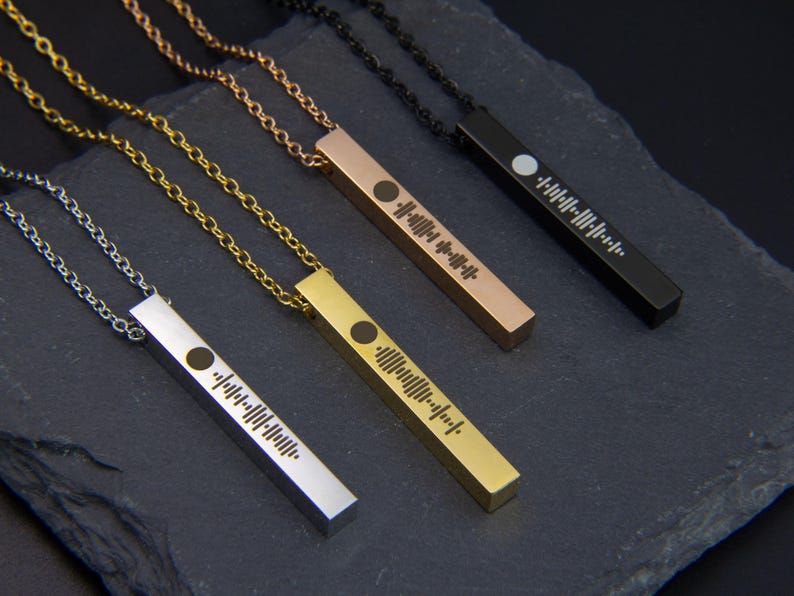 May include: Four necklaces with different coloured chains and bar pendants featuring a unique soundwave design. The chains are silver, gold, rose gold, and black.