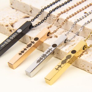 May include: Four bar necklaces with different coloured metal finishes: black, rose gold, silver, and gold. Each bar has a unique barcode-like design engraved on it.