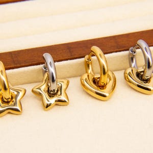 May include: Four gold hoop earrings with different charms. Two earrings have a star charm, one has a heart charm, and one has a heart charm with a smaller heart inside.
