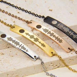May include: Three silver, gold, and black necklaces with a bar pendant featuring a unique soundwave design. Each pendant has a small circle in the center.