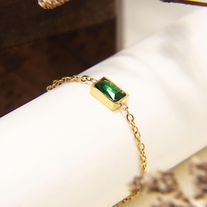 Puede incluir: Un delicado brazalete de cadena dorada con una sola piedra rectangular de color verde esmeralda.