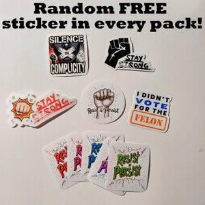 May include: A collection of stickers with various designs and text. The stickers include phrases like "Stay Strong," "Resist & Persist," and "I Didn't Vote for the Felon." The image also includes the text "Random FREE sticker in every pack!"