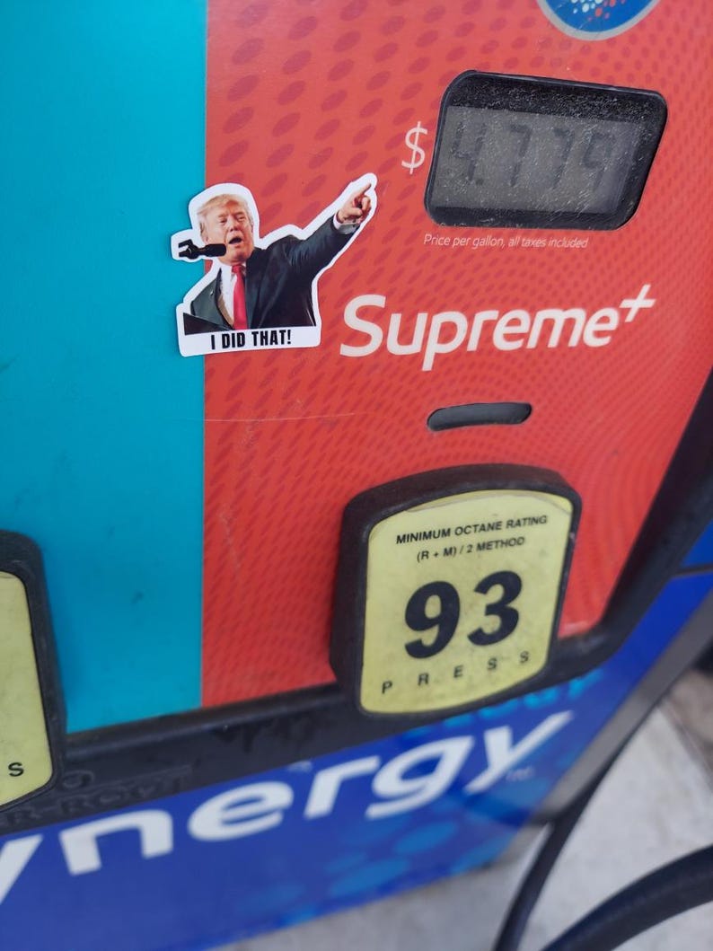 May include: A sticker of a man pointing, with the text "I DID THAT!" is placed on a red and blue gas pump. The pump displays a price of $4.779 per gallon. The brand "Supreme+" is visible.