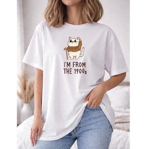 May include: White t-shirt featuring a cartoon cat wearing glasses, a scarf, and holding a cane. The text "I'M FROM THE 1900s" is printed below the cat. The shirt is paired with blue jeans.