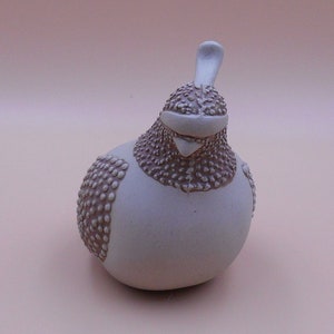 May include: A white ceramic bird figurine with brown speckled detailing. The bird has a rounded body and a small, pointed beak.
