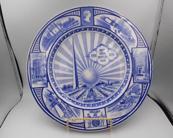 May include: Blue and white ceramic plate with a design commemorating the 1939 New York World's Fair. The plate features a central image of the Trylon and Perisphere, surrounded by smaller images of various fair exhibits. The text "New York World's Fair 1789-1939" is printed on the plate.