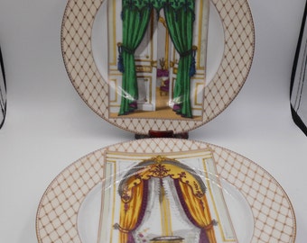 May include: Two decorative plates with a gold rim and a cream-colored diamond pattern border. The center of each plate features a detailed illustration of a room with curtains and a window. One plate has green curtains, the other has yellow.
