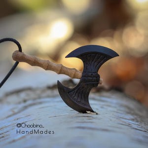 Könnte beinhalten: Ein handgefertigter Miniatur-Axtanhänger mit dunkler Klinge und hellem Holzgriff. Die Axt hängt an einer schwarzen Kordel. Der Hintergrund ist unscharf, mit dem Text "@Choobino_HandMades" sichtbar.