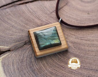 May include: A square wooden pendant with a green and blue labradorite gemstone set in the center. The pendant is on a brown leather cord.