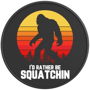 May include: A round, black graphic with a Bigfoot silhouette against a sunset backdrop of orange, yellow, and red. The text "I'D RATHER BE SQUATCHIN" is displayed in white, bold letters.