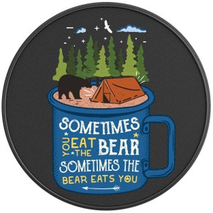 May include: A blue camping mug with the text "Sometimes you eat the bear, sometimes the bear eats you". The mug is filled with a brown liquid and a tent and a bear are on top of the mug.