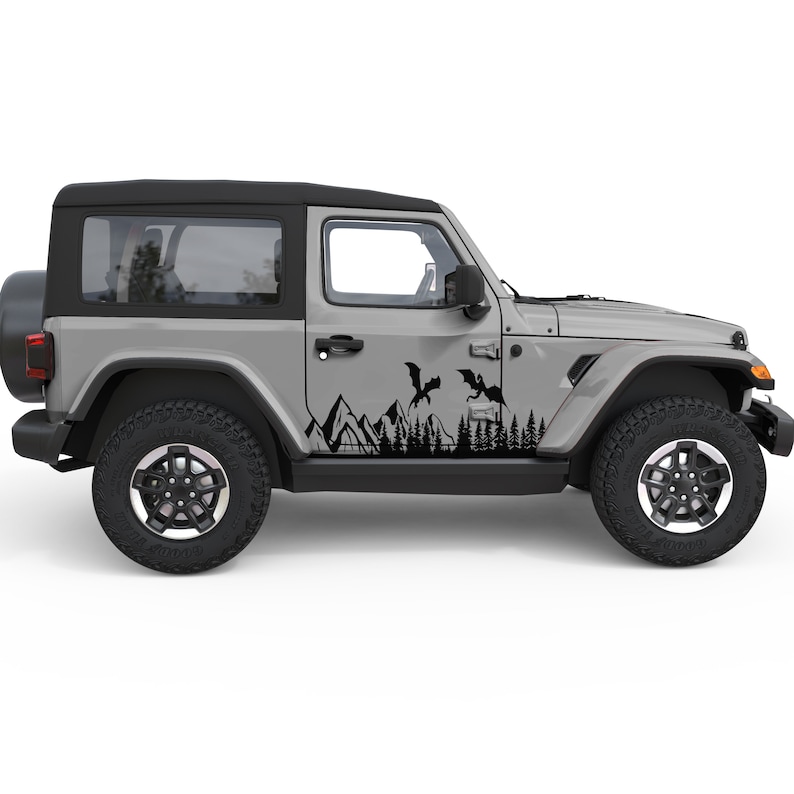 Puede incluir: Un Jeep Wrangler gris con calcoman&iacute;as negras de monta&ntilde;as, &aacute;rboles y dragones en el lateral.