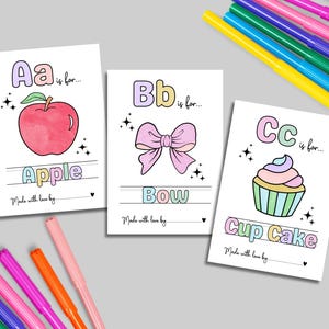 Puede incluir: Tres tarjetas ilustradas del alfabeto con las letras A, B y C. La tarjeta A presenta una manzana roja, la tarjeta B un lazo rosa y la tarjeta C una magdalena. Hay rotuladores de colores esparcidos alrededor de las tarjetas.
