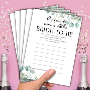May include: A stack of white paper cards with the text "My favourite memory with the BRIDE-TO-BE" in black script. The cards have a watercolor eucalyptus and gold leaf design. The cards are held by a hand.