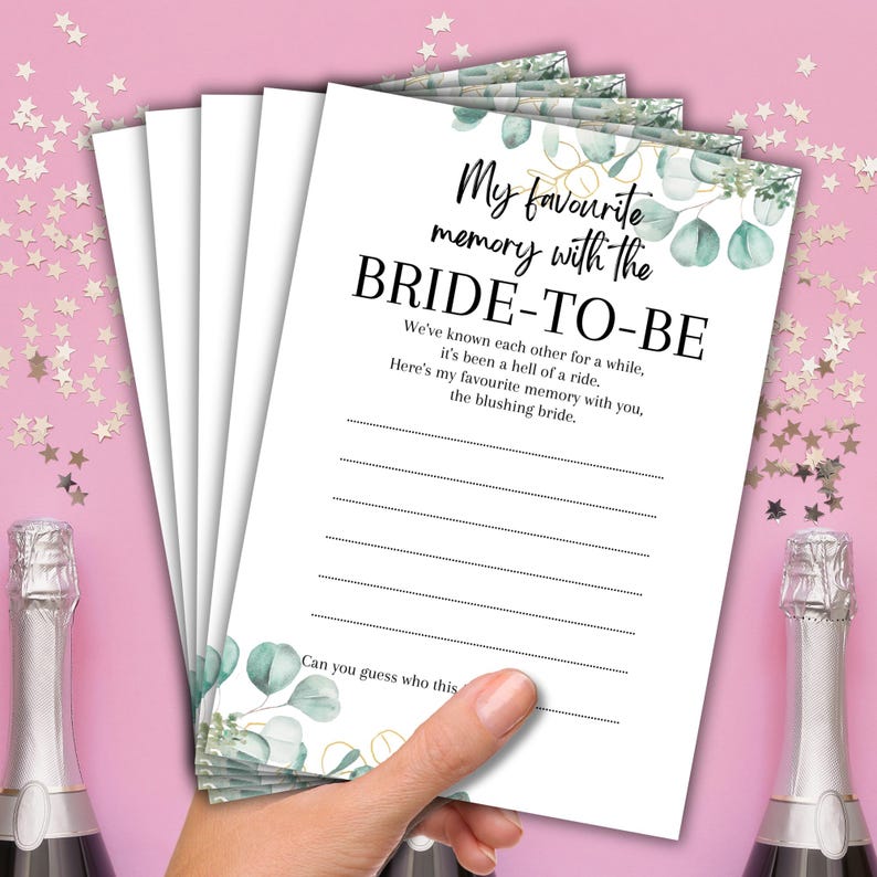 May include: A stack of white paper cards with the text "My favourite memory with the BRIDE-TO-BE" in black script. The cards have a watercolor eucalyptus and gold leaf design. The cards are held by a hand.