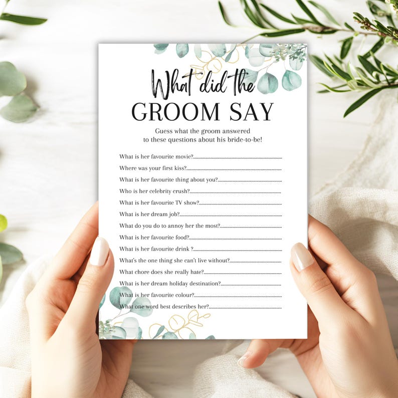 May include: A white bridal shower game card with the text "What did the GROOM SAY" in black script. The card features a list of questions for the groom to answer about the bride-to-be, with eucalyptus and gold accents.