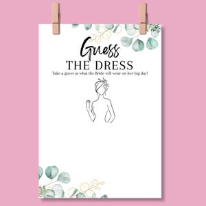 May include: A white paper sign with the text "Guess the Dress" in black script. The sign includes a line drawing of a bride and is decorated with watercolor eucalyptus leaves and gold accents. The sign is held by two wooden clothespins.