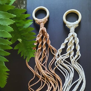May include: Two macrame plant hangers with wooden rings. One is beige and the other is a light brown colour. Both have wooden beads.