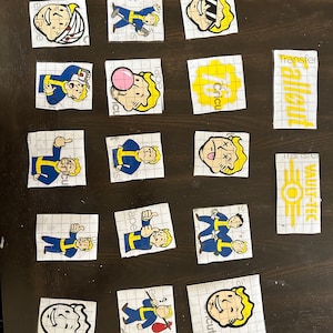 May include: A collection of 15 Fallout themed stickers featuring various characters and logos. The stickers are printed on clear sheets with a grid pattern. The stickers include characters with different expressions, poses, and accessories. The stickers also include the Fallout logo and the Vault-Tec logo.