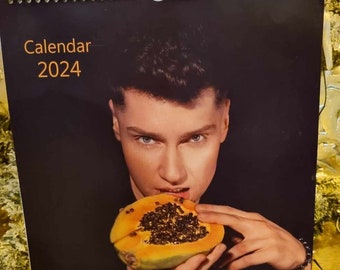 Op de afbeelding: Een kalender voor 2024 met een zwarte achtergrond waarop een persoon in een papaja bijt. De tekst "Kalender 2024" en "Sinful sweets" staat op de kalender gedrukt.
