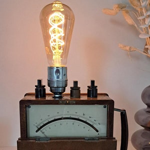 Może przedstawiać: Drewniana skrzynka w stylu vintage z okrągłym analogowym miernikiem i żarówką na górze. Skrzynka ma uchwyt i trzy pokrętła. Miernik ma skalę od 0 do 100.