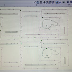May include: A computer screen displaying a design program with a white background and black lines. The design shows three identical shapes, each with a curved, rounded, and pointed end. The screen also shows a tool bar with icons for different functions. The text on the screen reads "Toolpaths, Material Setup, Set, Home Pos, Toolpath Operations, Sheet 1, Drill, Pocket, Cam, Cutout".