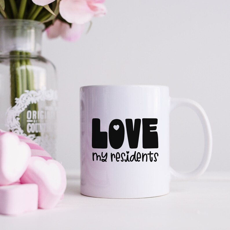 K&ouml;nnte beinhalten: Wei&szlig;e Keramik-Kaffeetasse mit einer schwarzen Grafik, auf der "LOVE my residents" mit einem kleinen Herzen in der Mitte des Wortes LOVE steht.