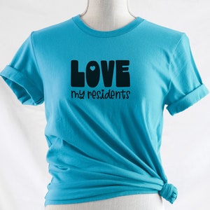 K&ouml;nnte beinhalten: Ein t&uuml;rkisfarbenes T-Shirt mit dem Text "LOVE my residents" in schwarzen Buchstaben mit einem kleinen blauen Herzen im "O".